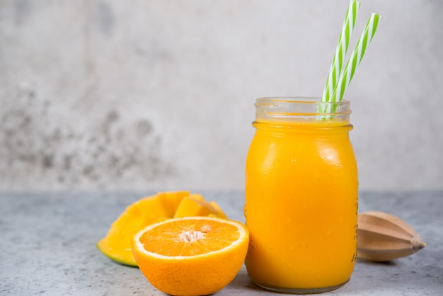 Mango smoothie with orange in a jar and with tubes stands on a gray concrete wall. Clean and healthy food for vegetarians. Healthy diet. Horizontal orientation.