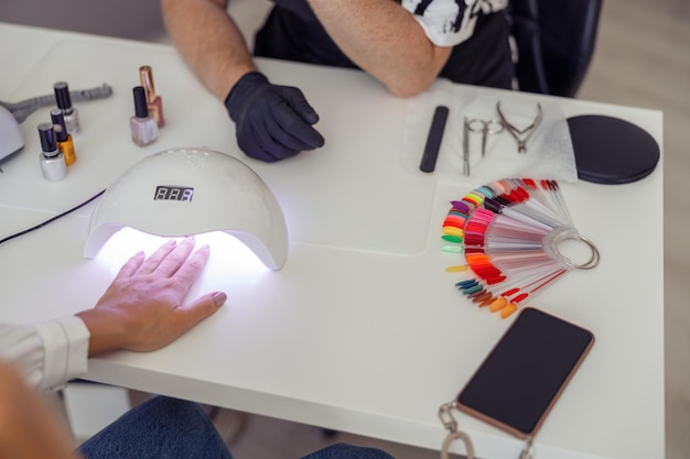 Manicure master doing nail care for client in work studio