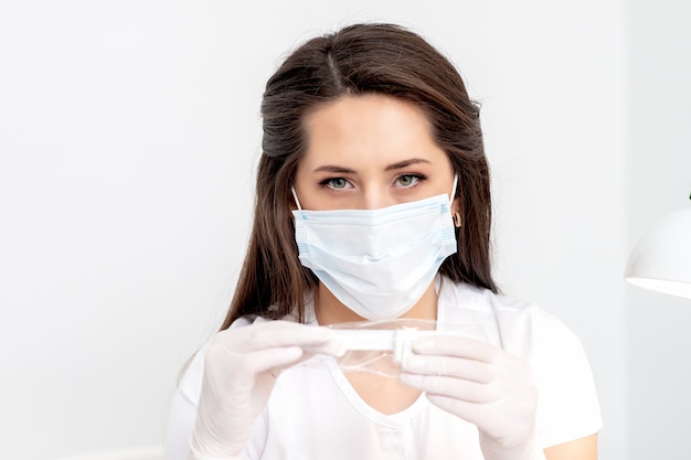 Manicure master with a mask on her face holding a manicure tool on a white background.