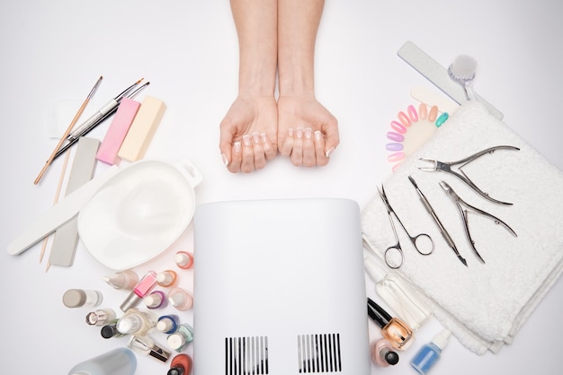 Manicure and pedicure items - nail polish drying lamp, nail file, scissors and brushes over light surface.