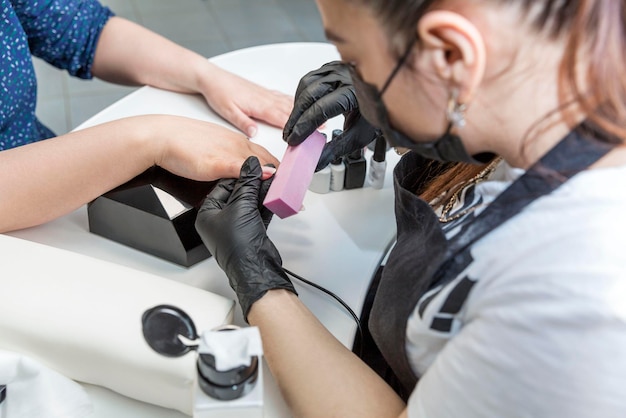 Manicure procedure in a beauty salon Master in black gloves and mask and the hands of the client Personal care and cosmetics