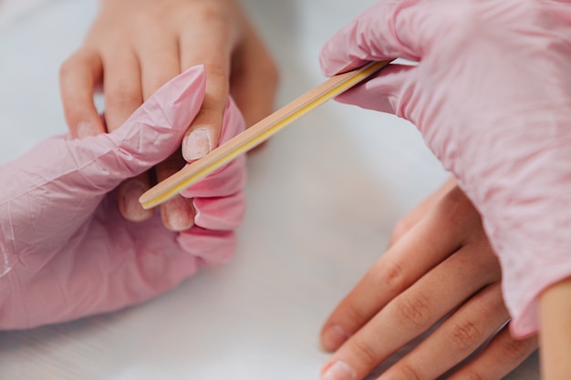 Manicure process. A master in pink rubber gloves processes the nails with a nail file. Female hands close up.