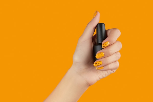 Manicured womans hand holding nail varnish bottle on orange background beauty salon template