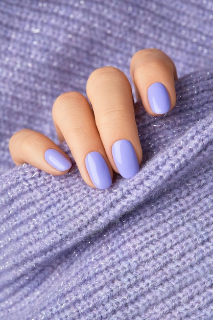 Manicured womans hand on violet knitted fabric Manicure pedicure beauty salon concept