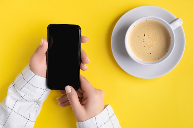 Manicured womans hands holding smartphone with blank screen. Flat lay, top view work at home office education concept.