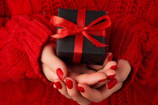 Manicured womans hands in red sweater holding gift box Christmas valentines day sale