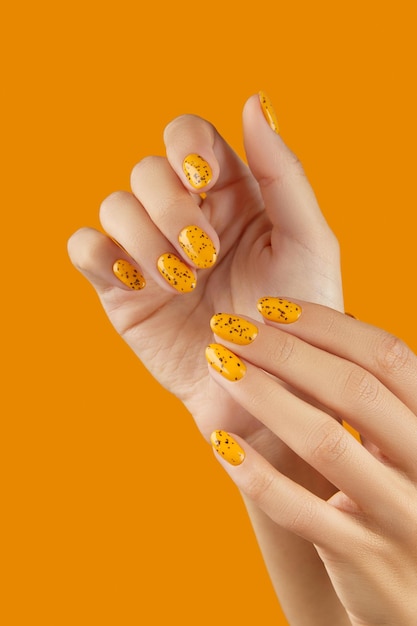 Manicured womans hands with trendy nail design on orange background