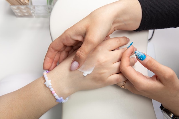 A manicurist applies hand cream to female hands after a hardware manicure in a beauty salon