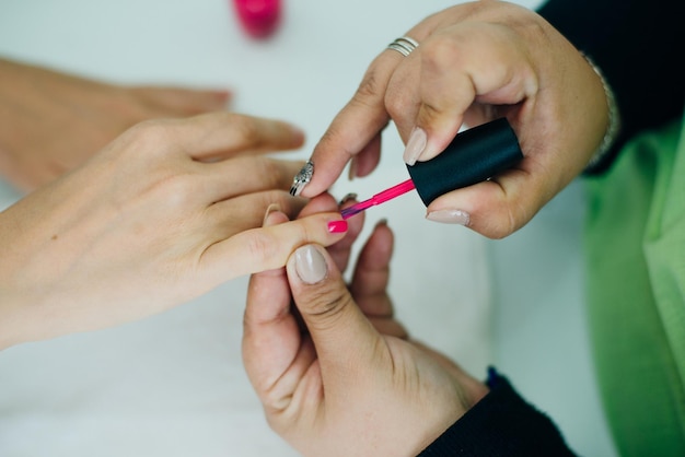 Manicurist applying pink nail varnish to the fingernails of a lady client in a spa or beauty salon