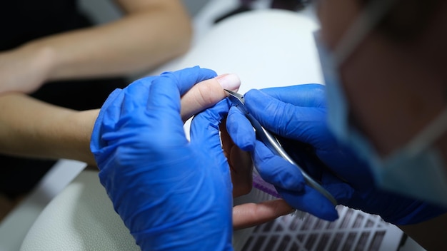 Manicurist in latex gloves cuts cuticle of clients finger closeup of working beautician in spa