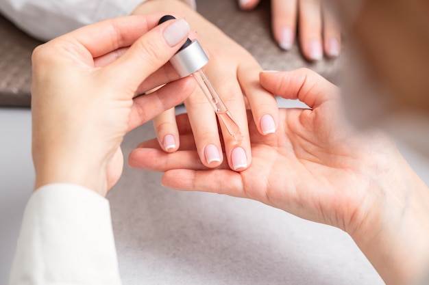 Manicurist pours oil on nails of woman