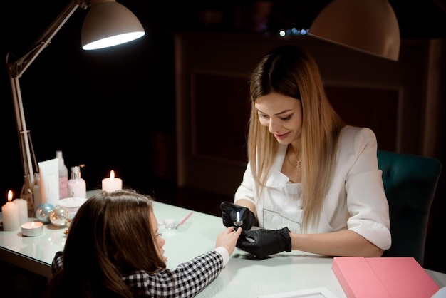 A manicurist in protective gloves paints a little girl's nails in a beauty salon