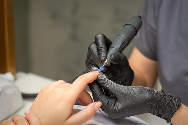 Manicurist removes nail polish uses the electric machine of the nail file during manicure in a nail salon.