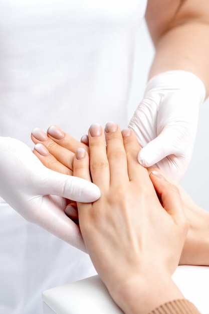 Manicurist wearing gloves doing wax massage on female hands with manicure in nail salon