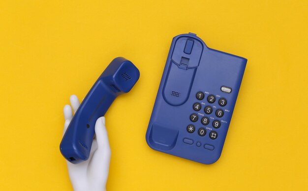 Mannequin hand holds office phone receiver on yellow background. Support phone, hot line