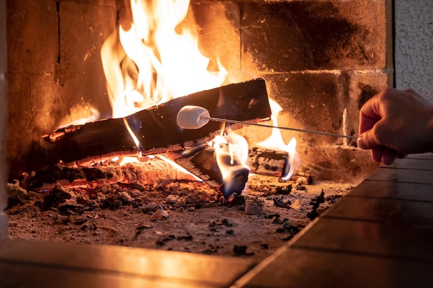 Mans hand fries a delicious sweet marshmallow on a fire in an open fireplace on a cold day