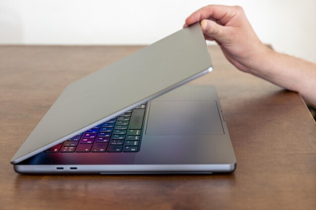 A mans hand opens a laptop with a multicolored glowing screen