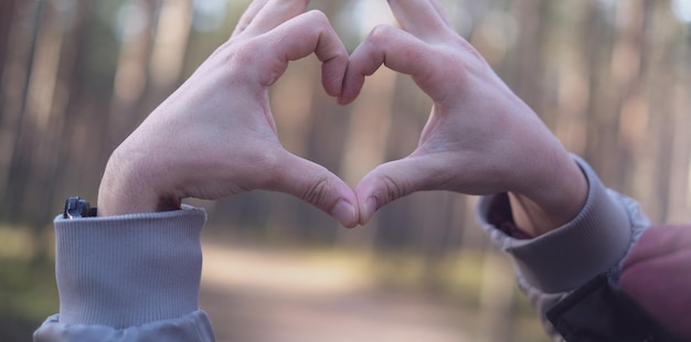 Mans hands folded into a heart symbolizing love and feelings against the backdrop of a forest