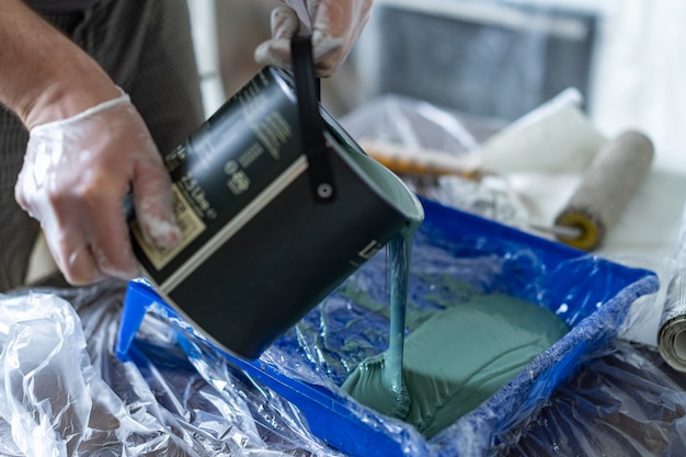 mans hands in rubber gloves  pouring green paint from bucket into tray