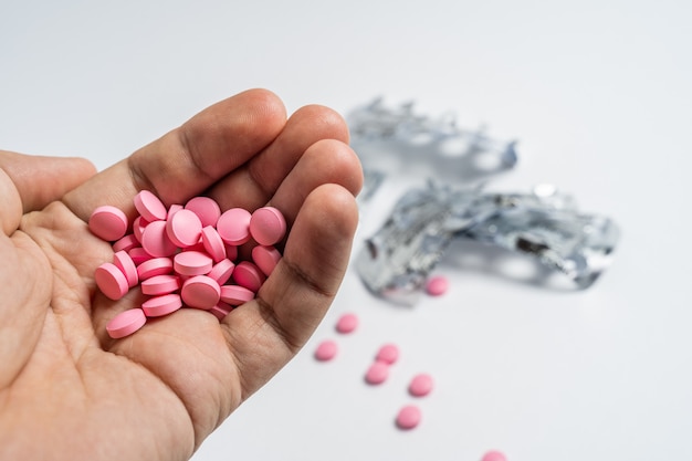 Mans hands with pills on, spilling pills out of bottle on white background