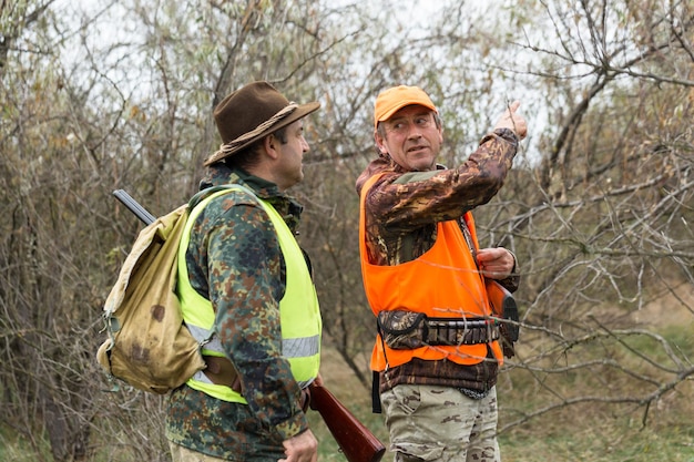 A mans with a gun in his hands and an orange vest on a pheasant hunt in a wooded area in cloudy weather Hunters with dogs in search of game