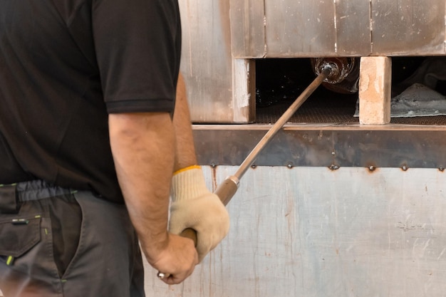 Manual glass production by glassblowing by worker at the factory man holding a vase in a muffle furnace