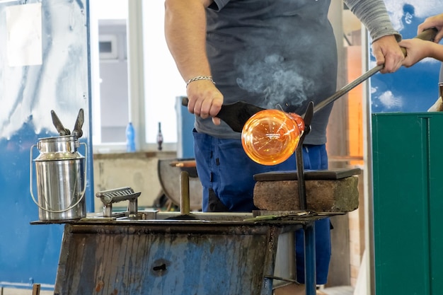 Manual glass production by glassblowing by worker at the factory