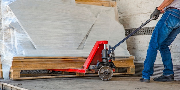 Manual loader. A forklift is towing a hand pallet truck. Folds and straightens the load in the truck before being shipped with a hand truck.