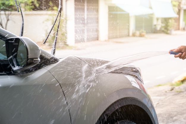 Manual washing car with pressure water hose on white car