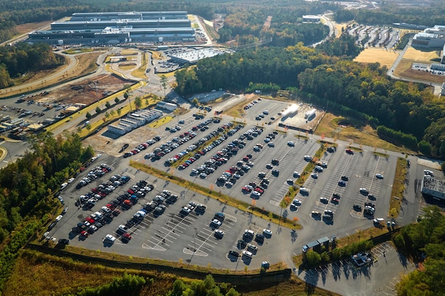 Many associate cars parked on big parking lot in front of industrial factory building Manufactoring and global industry concept