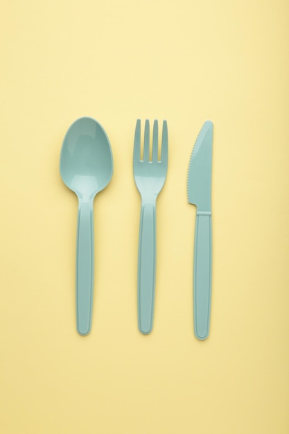 Many blue plasic forks spoons and knives on yellow background