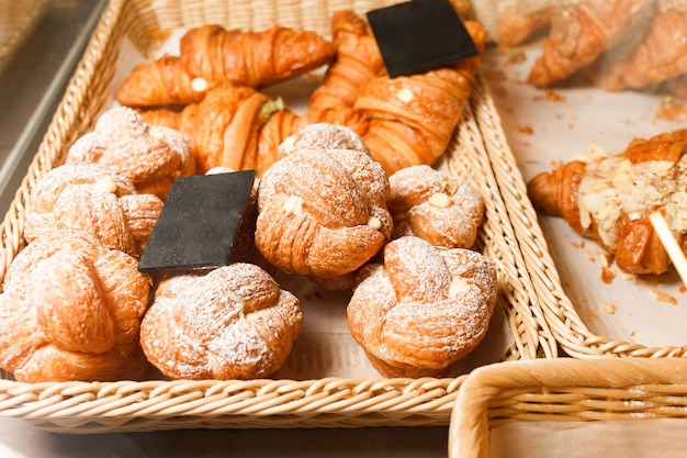 Many buns and croissants on a shelf of a baking shop