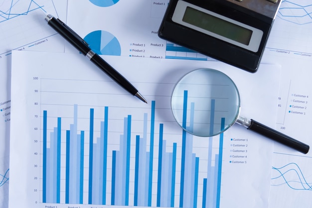 Many charts and graphs with magnifying glass and many pencil. Reflection light and flare. Concept image of data gathering and statistical working.