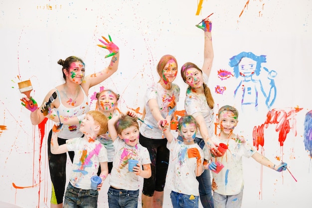 Many children and adults paint together with bright colors on the walls and on themselves