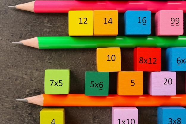 Photo many colorful cubes with numbers multiplications and pencils on dark grey table flat lay