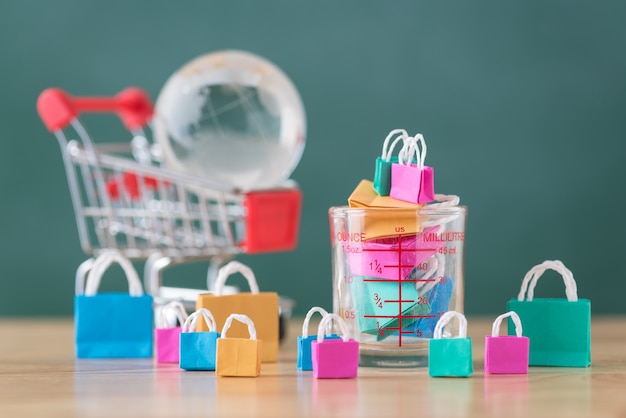 many colorful miniature shopping bags in measuring cup with cart and globe