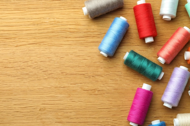 Many colorful sewing threads on wooden table flat lay Space for text