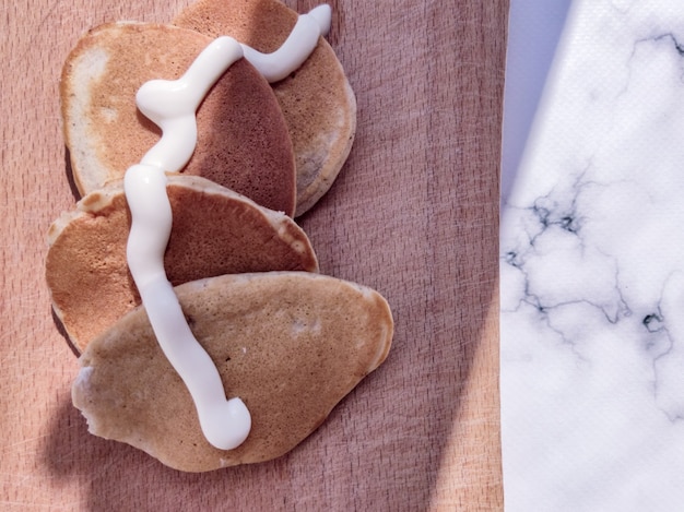 Many delicious appetizing pancakes with sour cream on a wooden board