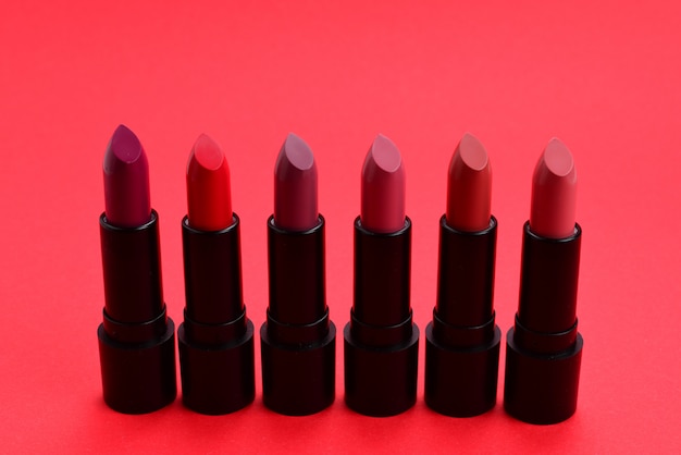 Many different lipsticks, different colors on red surface. Space for text or design.