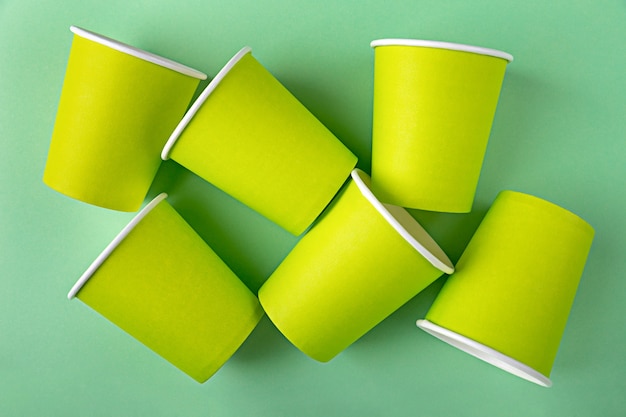 Many disposable empty mock up paper green cups for takeaway coffee or tea without lids flat lay on background