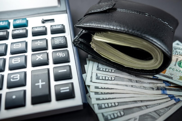 Many dollars appear from a dark wallet and a calculator on a plain background