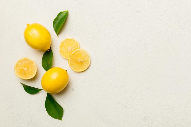 Many fresh ripe lemons with green leaves on colored background top view space for text