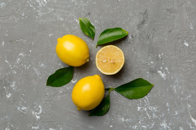 Many fresh ripe lemons with green leaves on colored background top view space for text