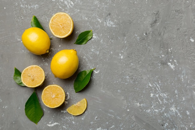 Many fresh ripe lemons with green leaves on colored background top view space for text