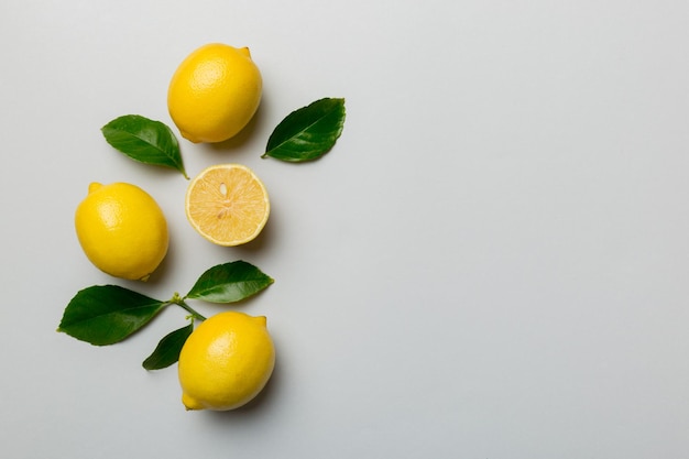 Many fresh ripe lemons with green leaves on colored background top view space for text