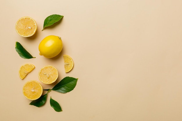 Many fresh ripe lemons with green leaves on colored background top view space for text