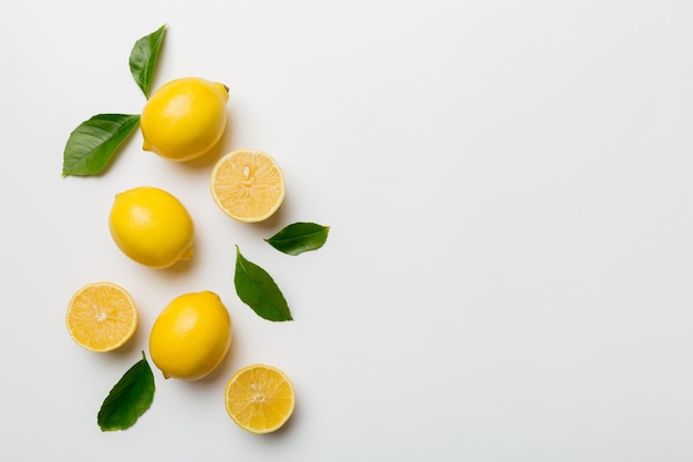 Many fresh ripe lemons with green leaves on colored background top view space for text