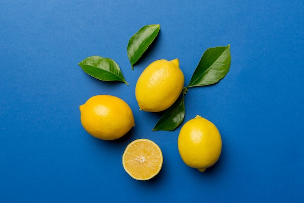 Many fresh ripe lemons with green leaves on colored background top view space for text