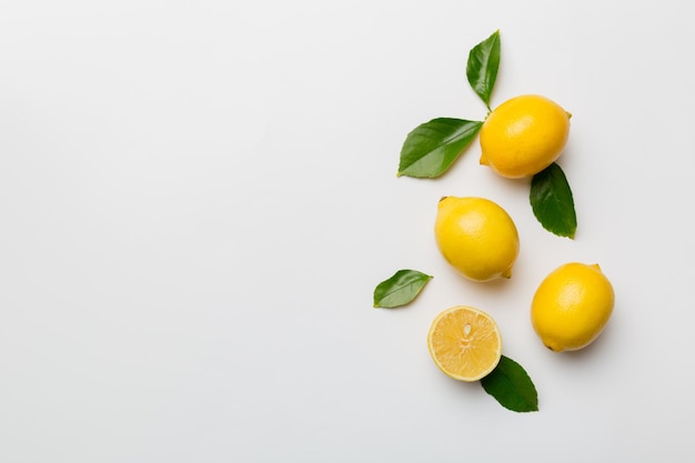 Many fresh ripe lemons with green leaves on colored background top view space for text