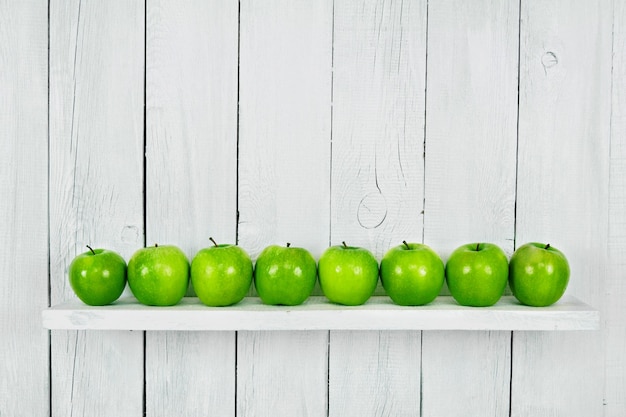 Many green apples on a shelf. A white, wooden background.